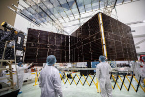 Technicians working beside one of the Psyche spacecraft's large solar arrays during launch preparations in Florida.