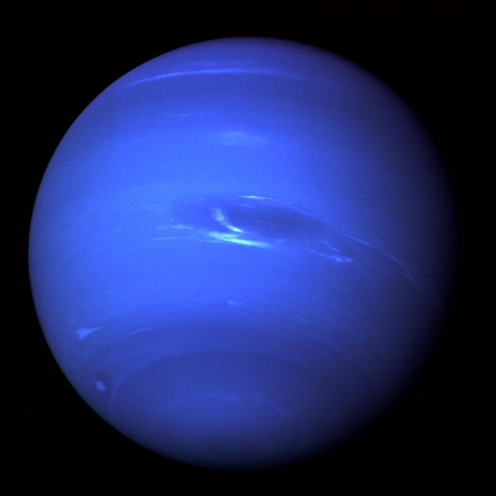 Neptune, a blue planet with a large dark storm spot and white streaks of cloud
