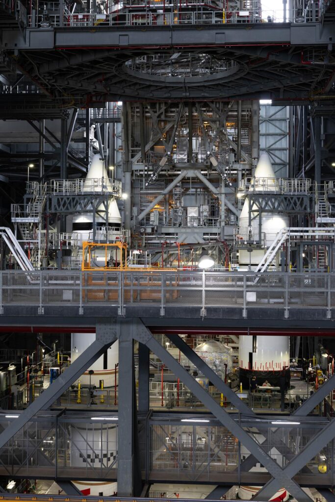 Two white SLS solid rocket boosters with nose cones standing inside the Vehicle Assembly Building